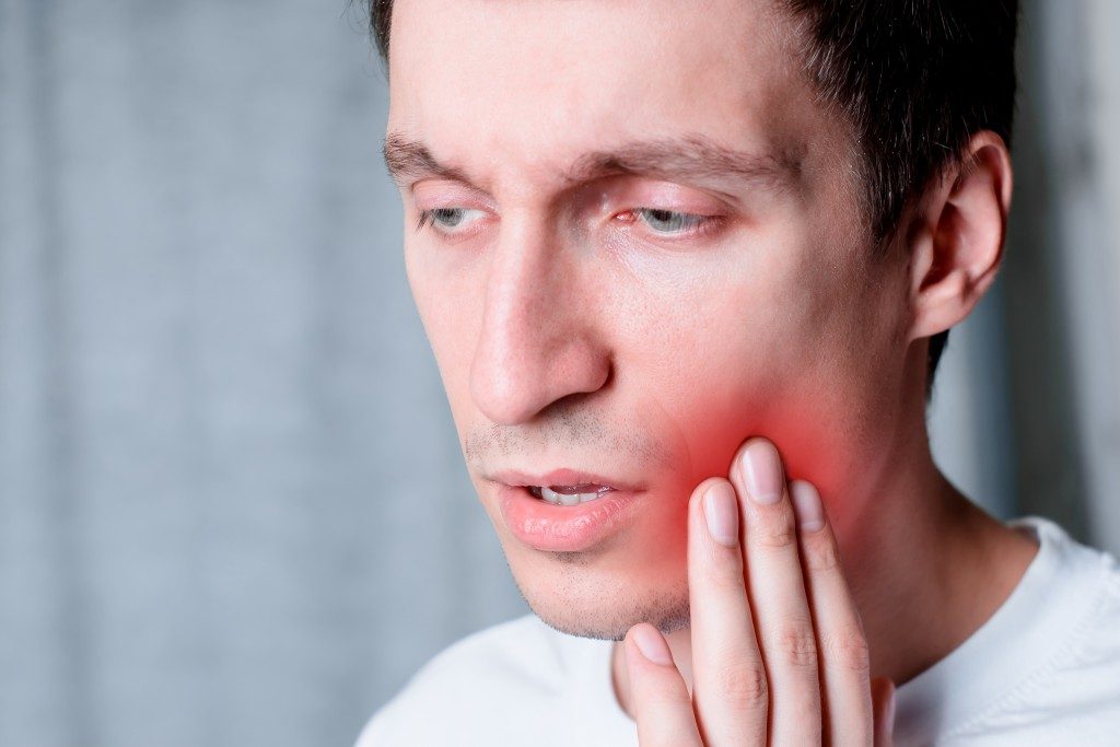 Man touching left cheek with a canker sore