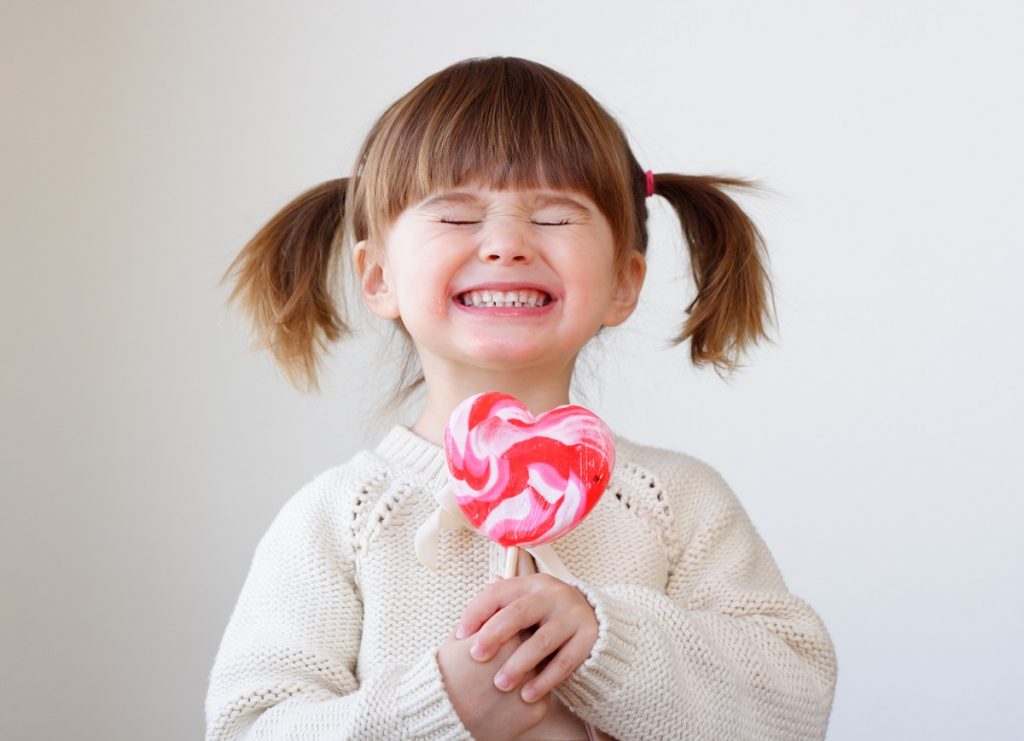 little kid smiling with a pink candy in hand