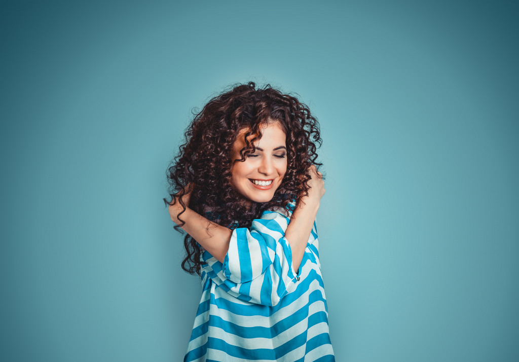 smiling woman hugging herself against blue background