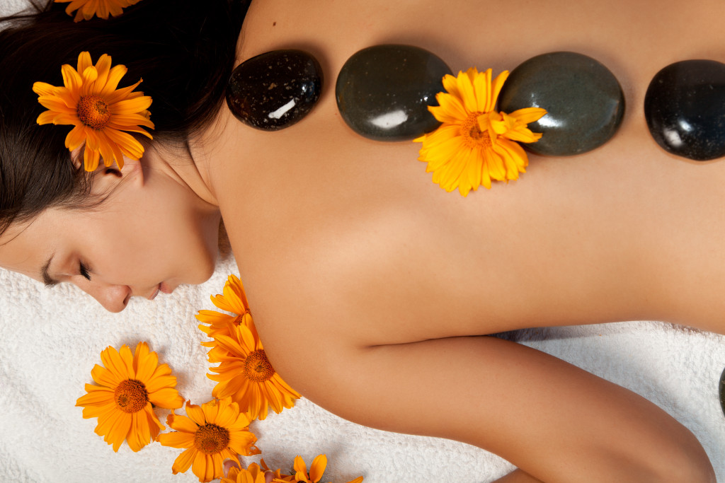 A woman lying down getting a hot stone massage with flowers sprinkled on her back